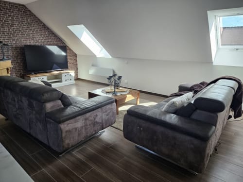 Spacieux salon loft au Cap à l'Ouest à Saint-Benoît-des-Ondes avec puits de lumière, deux canapés, téléviseur et décor bois