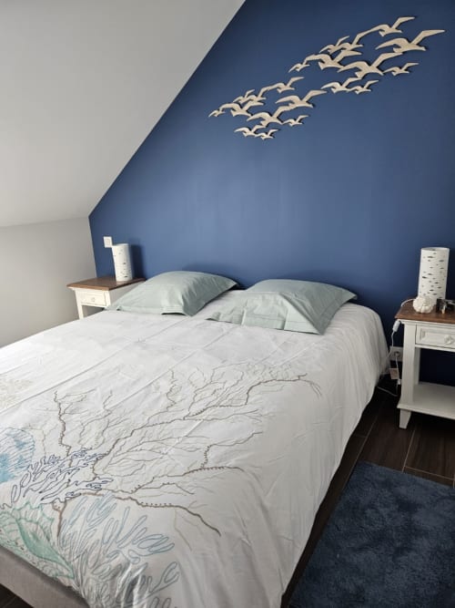 Chambre moderne du Clos de la Côte d'Émeraude avec mur bleu, décoration murale d'oiseaux et literie blanche à Cap-à-l'Ouest