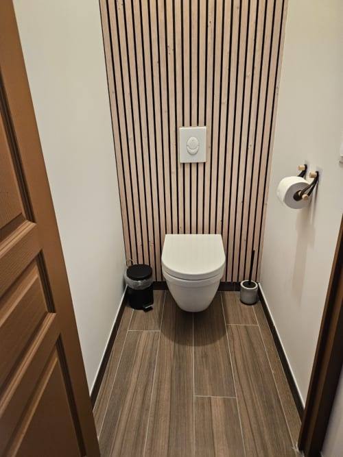 Salle de bains moderne avec murs en panneaux de bois vertical, bidet et sol en imitation bois, appartement Cap à l'Ouest au Clos De La
