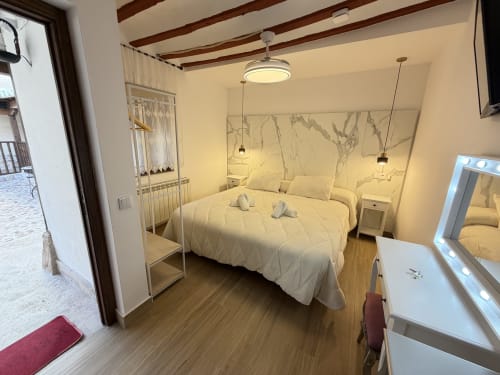 Modern bedroom at Complejo Turístico Retiro del Teatro in Almagro with cream bedding, marble headboard, wooden ceiling beams,