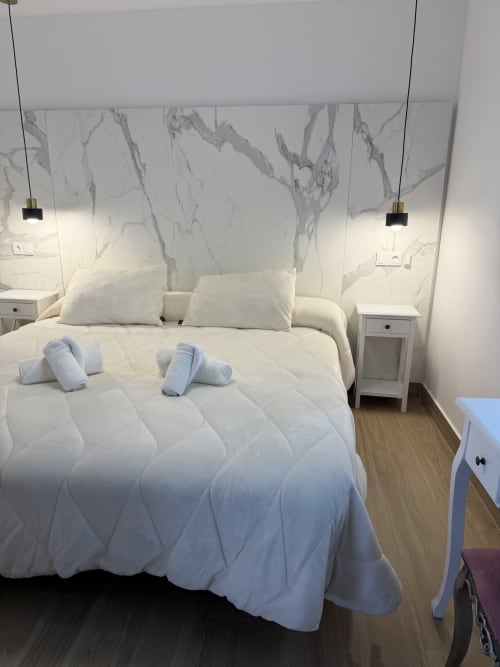 Modern bedroom at Complejo Turístico Retiro del Teatro with marble headboard, white bedding, and rolled towels in Almagro.