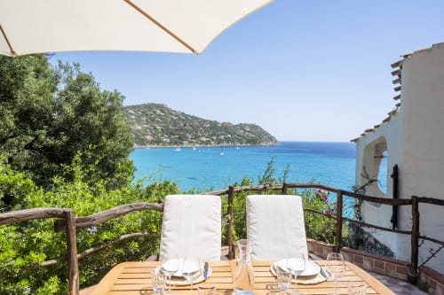 Terrazza di villa fronte mare in Sardegna con vista sul mare, tavolo da pranzo, lettini e costa mediterranea