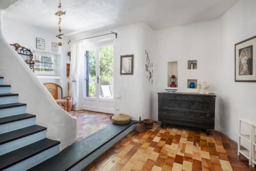 Ingresso luminoso con pavimenti in cotto, scala curva e comò in legno scuro - Top Villas Sardegna