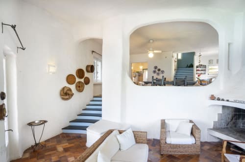 Luminoso soggiorno a Top Villas Sardegna con sedute in vimini, piatti decorativi, camino e scala con blu