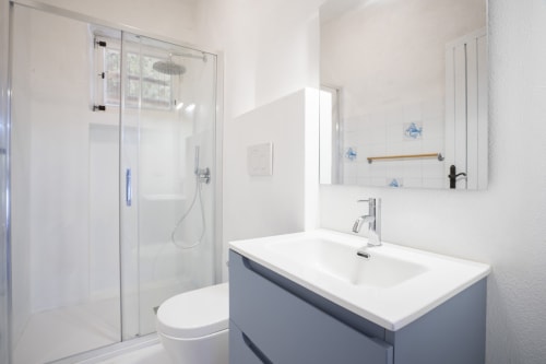 Bagno moderno a Top Villas Sardegna con piastrelle bianche, mobile azzurro, box doccia in vetro e specchio illuminato