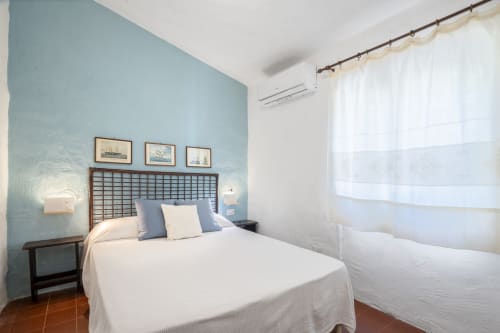 Camera luminosa alle Top Villas Sardegna con parete azzurra, letto matrimoniale, biancheria bianca e opere d'arte costiera a Quartu