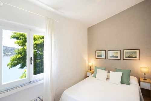 Camera da letto luminosa a Top Villas Sardegna con vista sul mare, biancheria bianca, cuscini verdi e opere d'arte nautiche