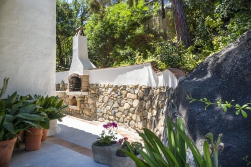 Camino esterno con base in pietra e muri bianchi a Top Villas Sardegna, circondato da piante in vaso e lussureggiante vegetazione