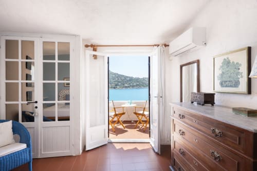 Camera da letto di villa sarda con balcone con vista mare, mobili in legno e paesaggio costiero a Top Villas Sardegna