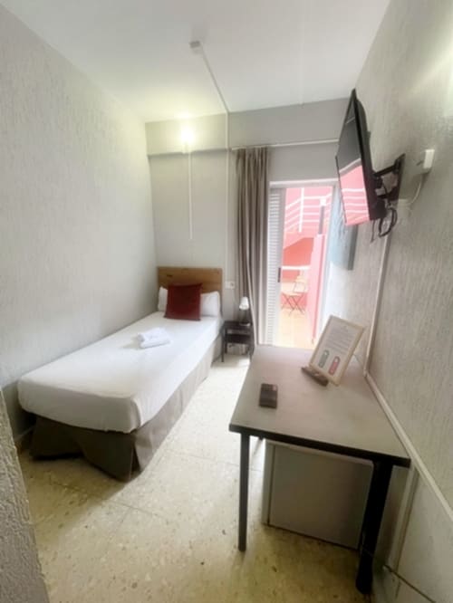 Compact hotel room at Hotel Don Cándido in Puerto de la Cruz with single bed, desk, TV, and terrace access with garden view