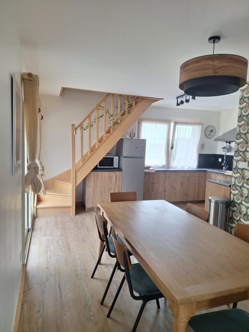 Open-plan kitchen and dining area in Gîte Kerroc'h cottage with wooden table, stairs, and modern appliances in Sizun, France