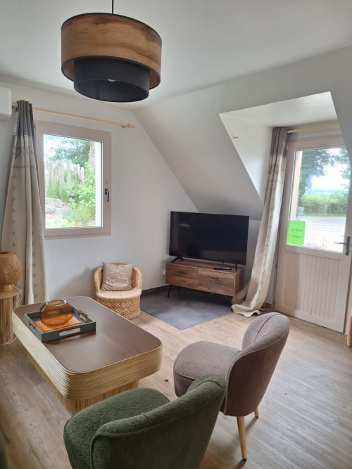 Modern cottage living room at Le Village Du Moulin with green chair, wooden TV stand, pendant light, and countryside views