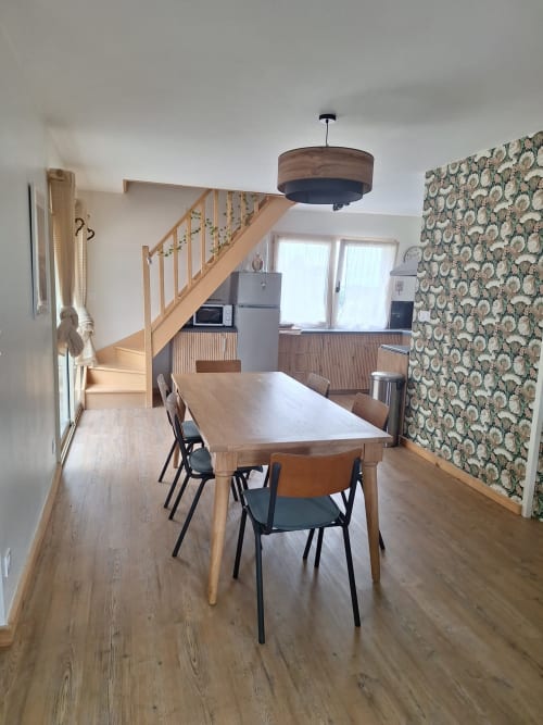 Spacious dining area in Gîte Kerroc'h cottage with wooden table, modern chairs, floral wallpaper, and staircase leading to