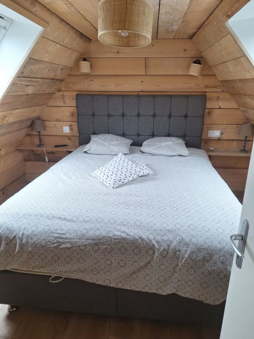 Cozy wooden cottage bedroom at Le Village Du Moulin with queen bed, dark headboard, and rustic beamed ceiling