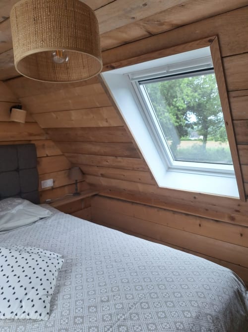 Cozy cottage bedroom with wooden beams, woven pendant light, and skylight overlooking Sizun countryside at Le Village Du