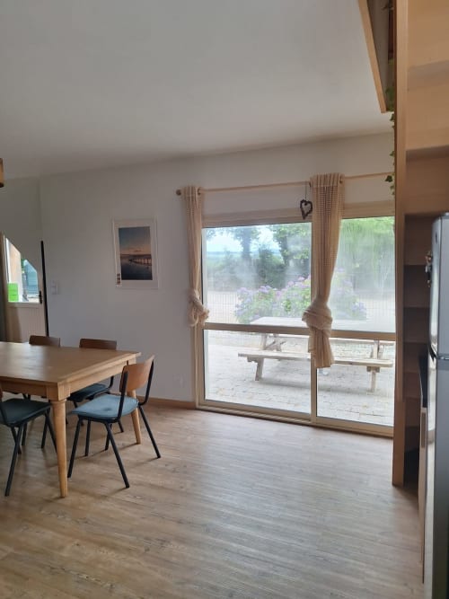 Bright dining area with wooden table and chairs, glass doors opening to garden terrace at Gîte Kerroc'h cottage, Sizun