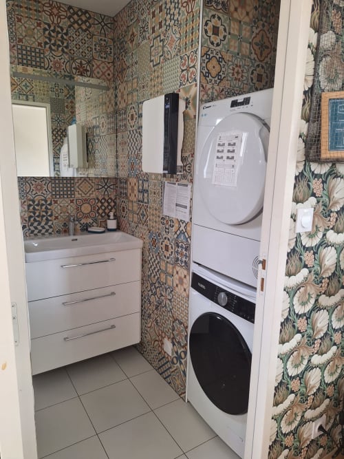 Modern bathroom with patterned tile walls, sink, stacked washer-dryer in cottage at Le Village Du Moulin, Sizun