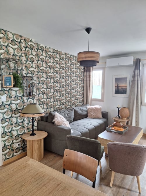Cozy living room at Gîte Kerroc'h cottage in Sizun with floral wallpaper, gray sofa, and wooden furnishings