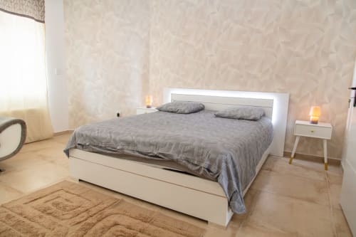 Chambre moderne de l'appartement Bali Room à La Valette du Var, avec lit blanc, linge de lit gris, murs beige texturés et vue sur le jardin
