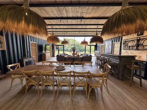Spacious cottage dining area at Le Village Du Moulin with wooden table, rattan chairs, and garden views through large windows