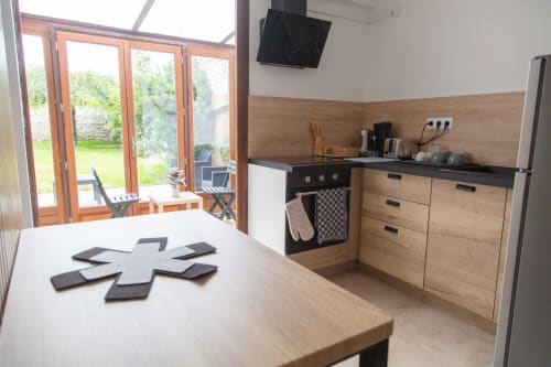 Cuisine moderne aux meubles en bois, plan de travail noir et portes donnant sur le jardin à la Maison Cosy à La Valette du Var
