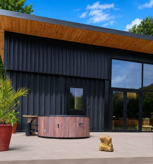 Modern black cottage with wooden overhang at Le Village Du Moulin, Sizun. Garden view with pool and terrace.