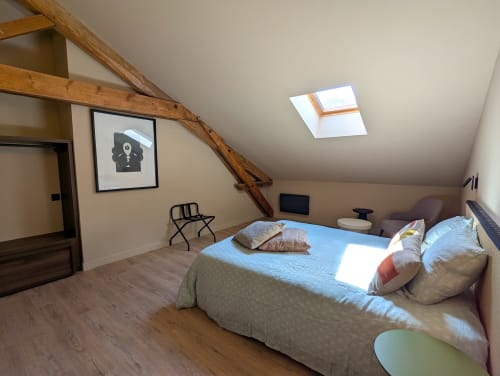 Chambre lumineuse sous les combles au Domaine Alga avec poutres apparentes, lucarne, linge de lit bleu et parquet