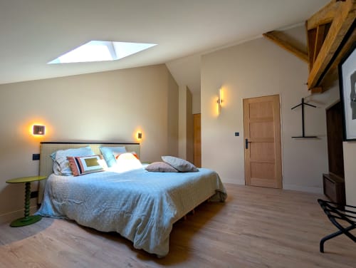Chambre mansardée moderne au Domaine Alga avec lucarne, poutres bois, literie bleue et éclairage ambiant chaleureux