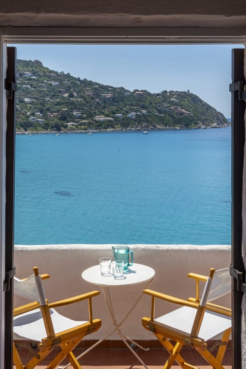 Villa sulla spiaggia in Sardegna con vista turchese, sedie in legno e case sulle colline