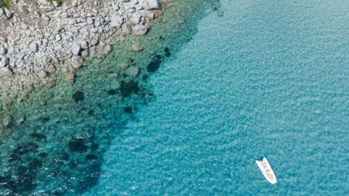 Vista aerea del mare turchese cristallino con barca bianca presso la costa rocciosa di Top Villas Sardegna