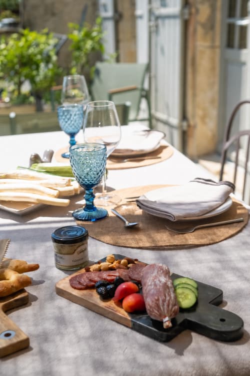 Table de dîner en plein air à La vie de château, Grignan, avec plateau de charcuterie, verres bleus, pain et vue sur les montagnes
