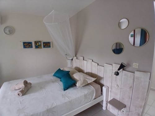 Studio bedroom at Ti Village Créole in Sainte-Anne with white bed, blue pillow, and garden view mirrors