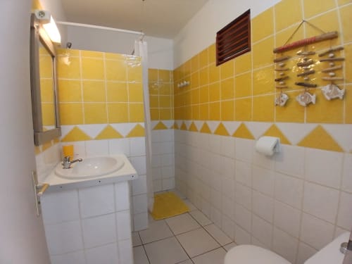 Bright bathroom with yellow and white tiles at Ti Village Créole, Sainte-Anne, featuring sink, shower, and toilet