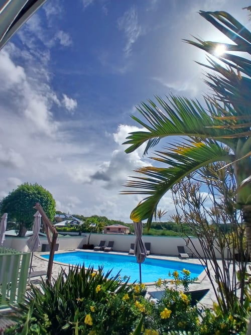 Ti Village Créole resort pool in Sainte-Anne with tropical palm trees, blue water, umbrellas, and garden views under clear