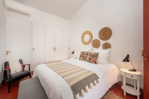 Quarto luminoso em Monte das Açoteias com cama branca, cestos de parede tecidos, piso de azulejo vermelho e vista para o jardim em Tavira, Portugal