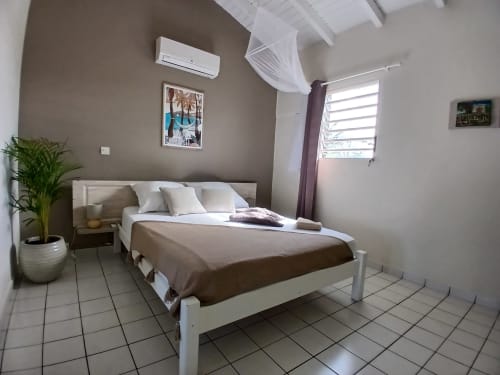 Bright bedroom at Ti Village Créole in Sainte-Anne with queen bed, white shutters, AC unit, and garden view