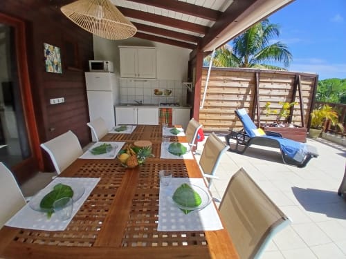 Ti Village Créole bungalow dining area with kitchen, set table, and terrace overlooking garden in Sainte-Anne