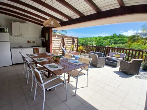 Spacieuse terrasse du bungalow à Ti Village Créole avec table à manger, coin détente, cuisine et vue sur jardin luxuriant