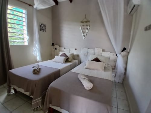 Two twin beds with white headboards in a bright bedroom at Ti Village Créole bungalow in Sainte-Anne, Guadeloupe