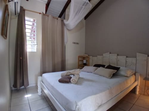 Bright bedroom in Ti Village Créole bungalow, Sainte-Anne, with queen bed, white headboard, ceiling fan, and garden view
