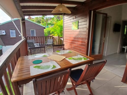 Terrasse couverte du bungalow Ti Village Créole avec table en bois, couverts et vue sur le jardin tropical