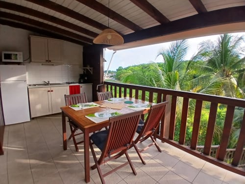 Covered terrace with dining table and chairs overlooking tropical garden at Ti Village Créole bungalow in Sainte-Anne,