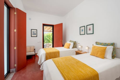 Quarto luminoso em Monte das Açoteias com camas geminadas, roupas de cama amarelas, portas vermelhas e vista para o jardim, Tavira, Portugal