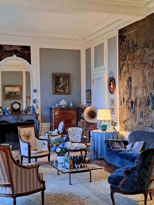 Élégant salon du Château de Tharoiseau avec mobilier d'époque, tapisseries historiques, cheminée et sièges en velours bleu