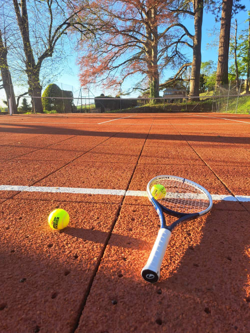 Raquette de tennis et balle sur le court de terre battue du Château de Tharoiseau, refuge à la campagne française