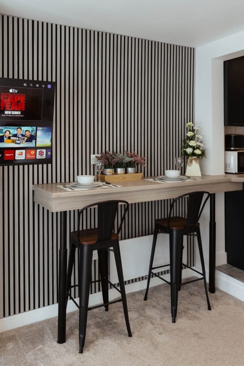 Modern breakfast bar with black stools at The Snug by JS Apartments Blackburn, featuring striped wall paneling and smart TV.