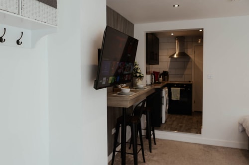 Modern kitchen area at The Snug by JS Apartments in Blackburn with wall-mounted TV, breakfast bar, and appliances