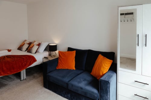 Modern studio apartment bedroom at The Snug, JS Apartments Collection in Blackburn, featuring bed with red throw, navy sofa