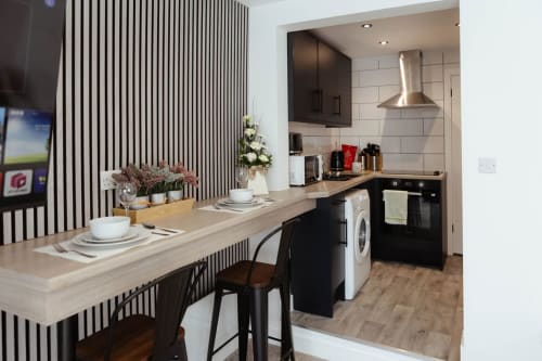 Modern kitchen and dining area at The Snug, JS Apartments Blackburn, featuring black cabinetry, breakfast bar, and stainless