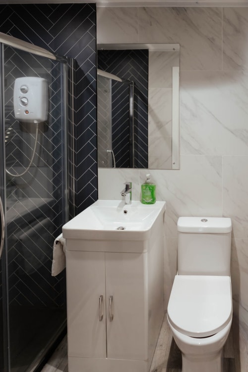 Modern bathroom at The Snug by JS Apartments Blackburn with black herringbone tiles, white sink vanity, toilet, and shower